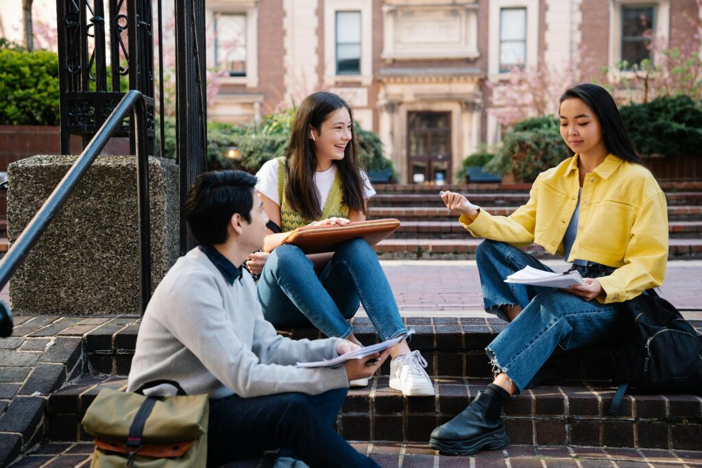 A group of college students sitting and discussing on university steps, engaging in lively conversation.